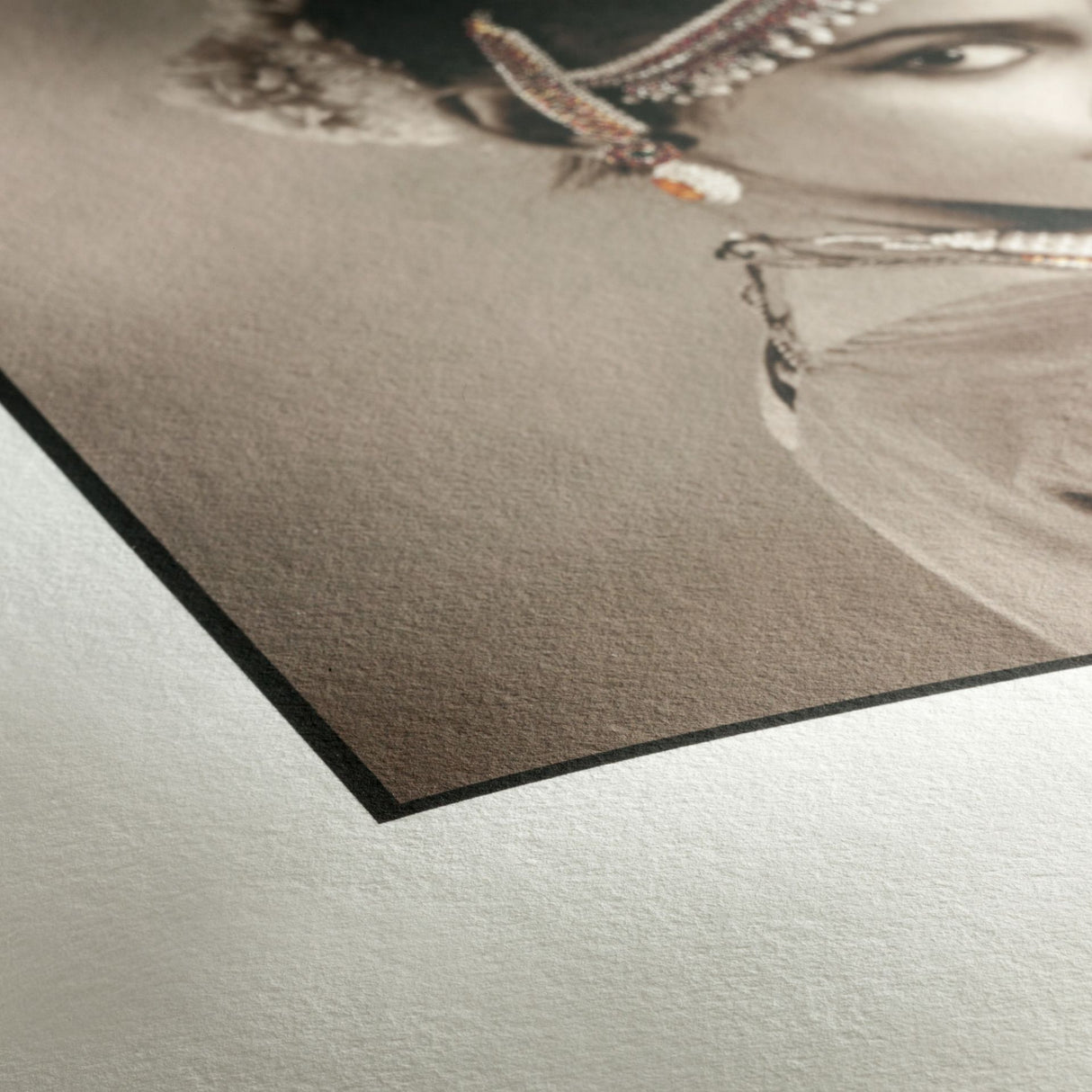 A close-up of the corner of a sepia-toned photo printed on Hahnemühle Photo Rag® (308) by Hahnemuhle, featuring part of a woman's face with beaded jewelry and showcasing the textured surface and edge typical of FineArt inkjet printing.