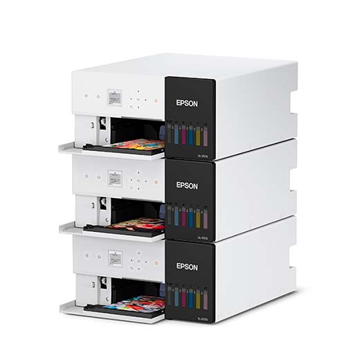 Three stacked Epson SureLab D570 Professional Minilab Photo Printers, each with visible ink tanks and open trays printing vibrant photo pages. Sleek white design with black accents—ideal for high-quality event photo printing.