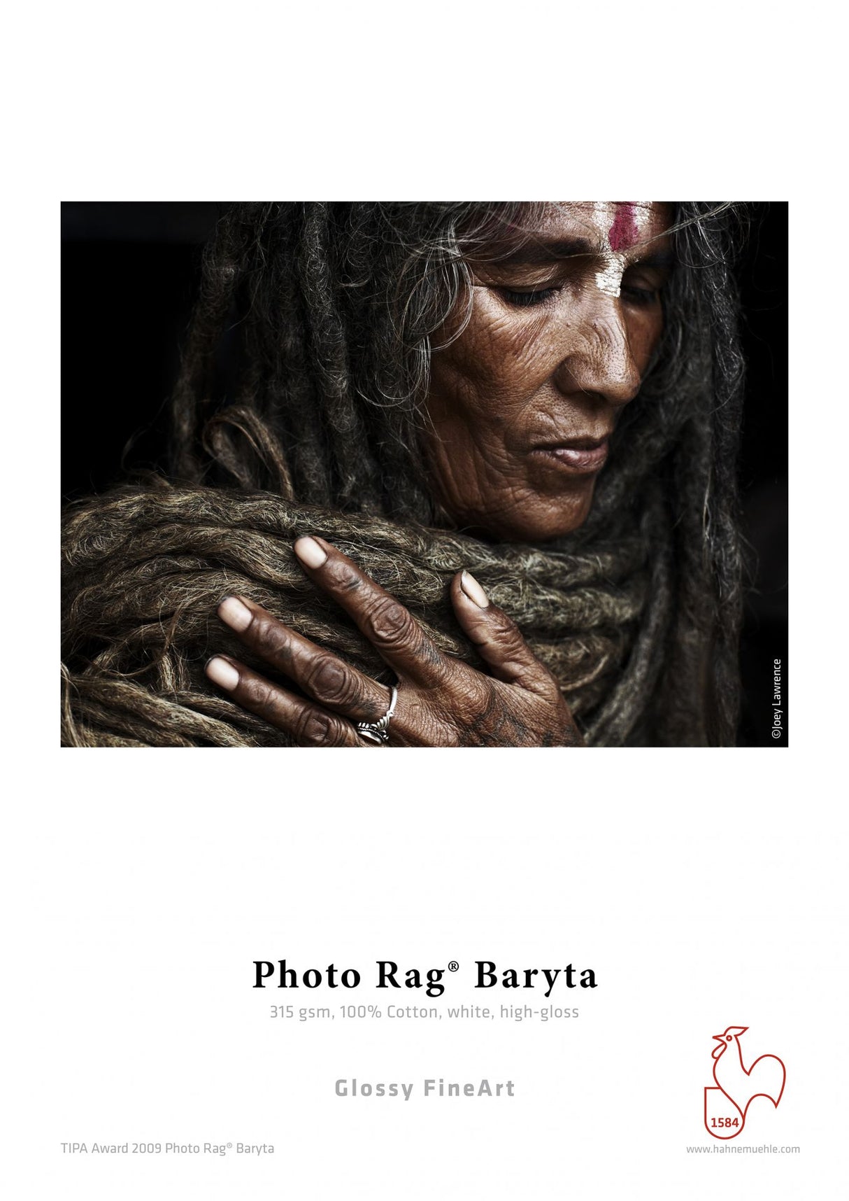 A close-up of a person with long, matted hair, dark skin, and a painted forehead gently touches their chest adorned with rings. Below is text about Hahnemühle Photo Rag® Baryta fine art cotton paper by Hahnemuhle.