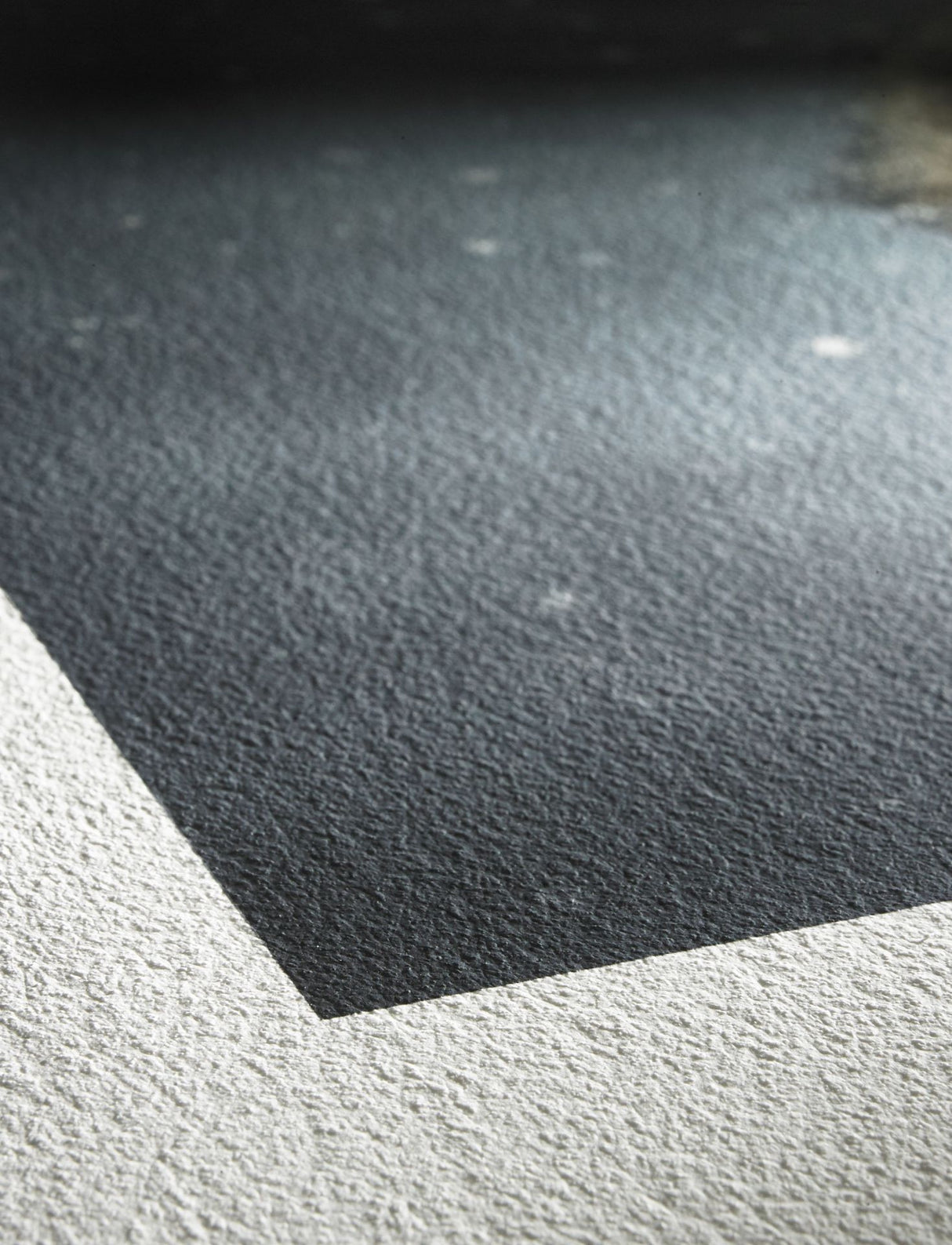 Close-up of a textured surface with a sharp, diagonal edge dividing dark and light gray areas, resembling Hahnemuhle William Turner 310 gsm fine art inkjet paper.