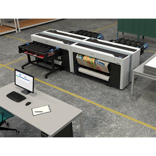 The Epson SureColor P8570D 44-Inch Wide-Format Dual Roll Printer by Epson is set up in an industrial workspace, ideal for professional wide-format photo printing. Nearby, a desk holds a monitor, keyboard, notepad, and pen.