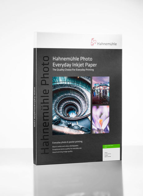 A box of Hahnemuhle Photo Pearl 310 photo paper with a gray design, product details, and images of a staircase, flower, and ferris wheel stands upright on a white surface.