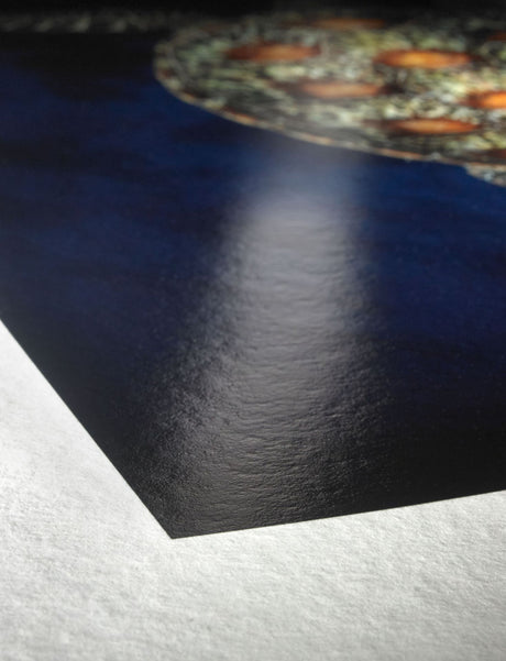 Close-up of the corner of a glossy, dark print on textured white Hahnemuhle Fine Art Baryta paper, featuring part of an intricate circular design in the upper right corner.