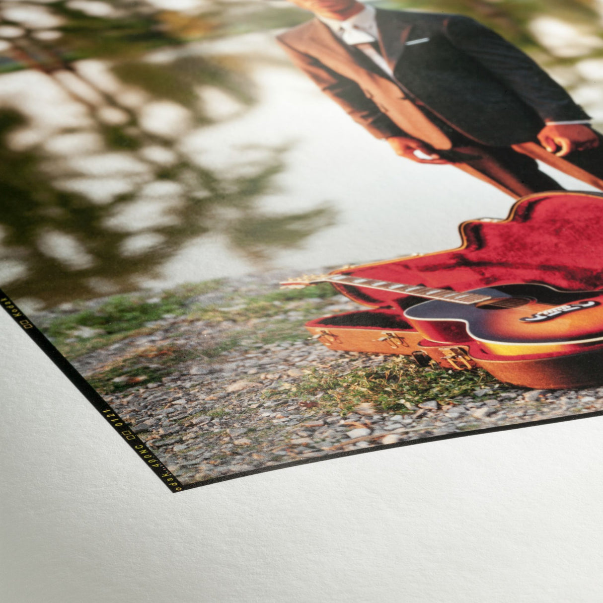 A photograph printed on Hahnemühle FineArt Pearl by Hahnemuhle features a person in a suit outdoors next to an open guitar case and guitar on gravel, with trees reflected in the background.