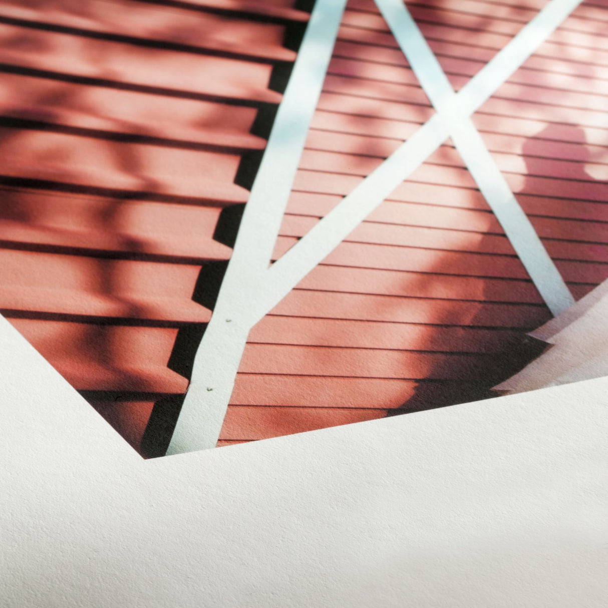 Close-up of a photograph on Hahnemuhle Photo Rag® Book & Album paper, featuring a red wooden surface with diagonal white beams and shadows. The image is partially cropped by a white border. Ideal for book and album creation.