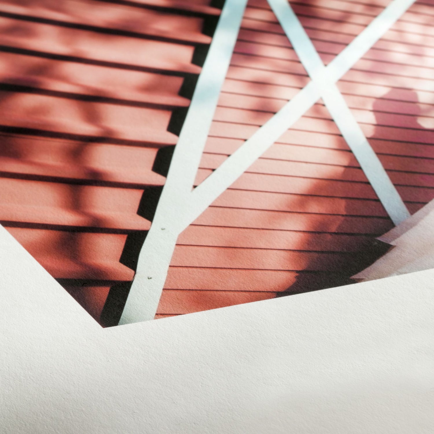 Close-up of a photograph on Hahnemuhle Photo Rag® Book & Album paper, featuring a red wooden surface with diagonal white beams and shadows. The image is partially cropped by a white border. Ideal for book and album creation.