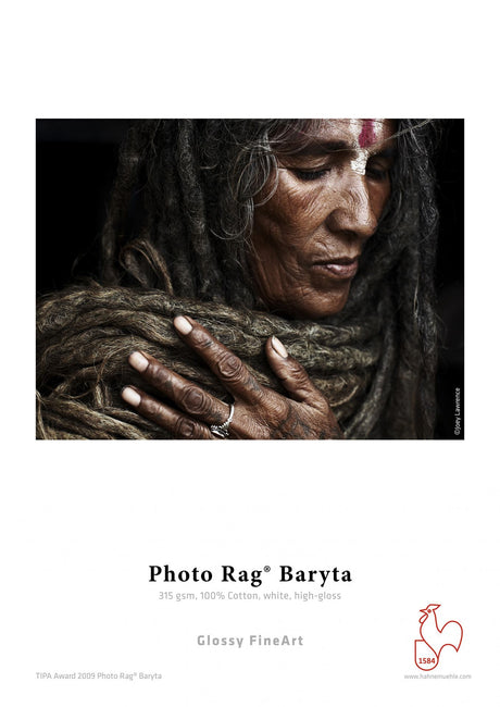 A close-up of a person with long, matted hair, dark skin, and a painted forehead gently touches their chest adorned with rings. Below is text about Hahnemühle Photo Rag® Baryta fine art cotton paper by Hahnemuhle.