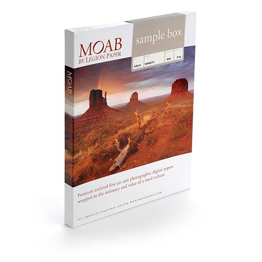 The MOAB Moab Sample Box - 8.5”x11” (2 sheets of each paper) stands upright, featuring a desert landscape with rock formations on the cover and text at the top describing included fine art and photo paper samples.